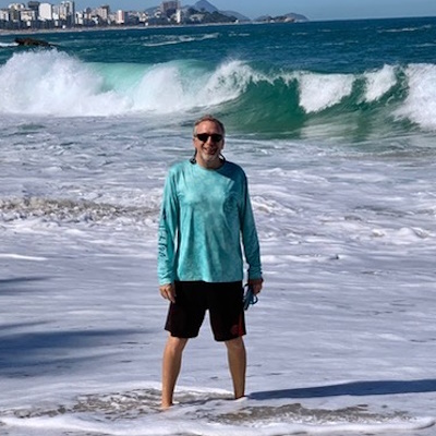 Professor Emeritus Ken Gouwens standing on a sunny beach with ocean waves, looking incredibly happy.