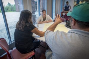 Three people at a table in front of a window having a discussion. (Sean Flynn/UConn Photo)