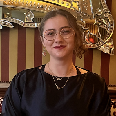 UConn grad student Brigitte Lewis smiling in front of a red and gold striped wall and ornate gold mirror