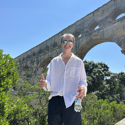 MA student Max DeLoach smiling and giving a thumbs up in front of an aqueduct